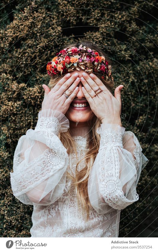Glückliche Braut bedeckt Augen in der Nähe des Buschwerks Frau Garten Lächeln Augen abdecken Buchse grün Sommer Hochzeit jung hochzeitlich Kleid geblümt