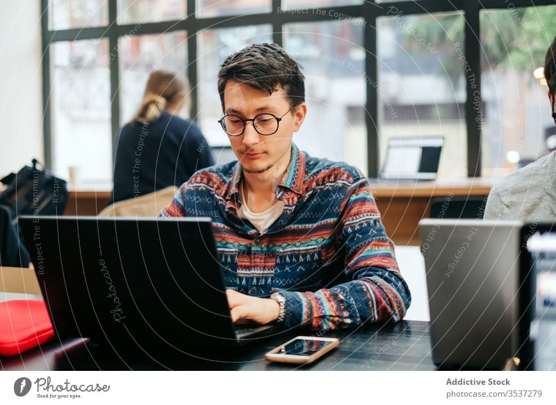 Fokussierter Arbeiter mit Laptop im Büro Mann Tippen intelligent Arbeitsplatz professionell Arbeitstag Smartphone Projekt Brille lässig Schreibtisch benutzend