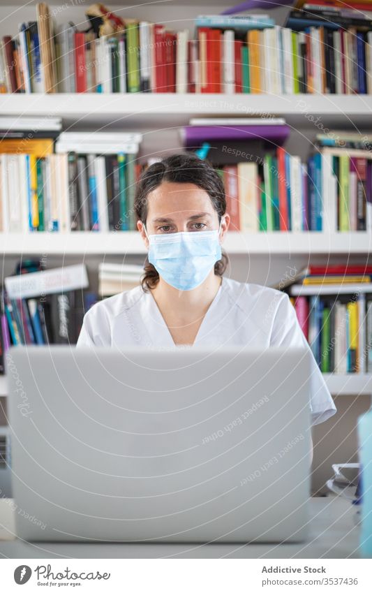Junge Ärztin mit medizinischer Maske arbeitet am Laptop in der Klinik Frau Arzt Uniform Mundschutz Handschuh Schreibtisch ernst Krankenhaus professionell