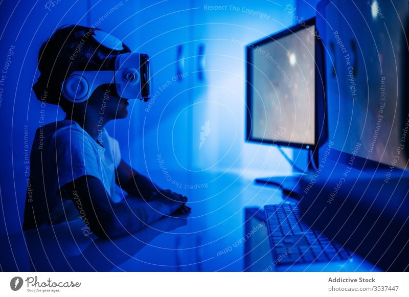 Unbekannter Junge im VR-Headset vor dem Computer sitzend Desktop Monitor Entertainment Video benutzend Gerät Apparatur Brille Drahtlos zuschauen Bildschirm