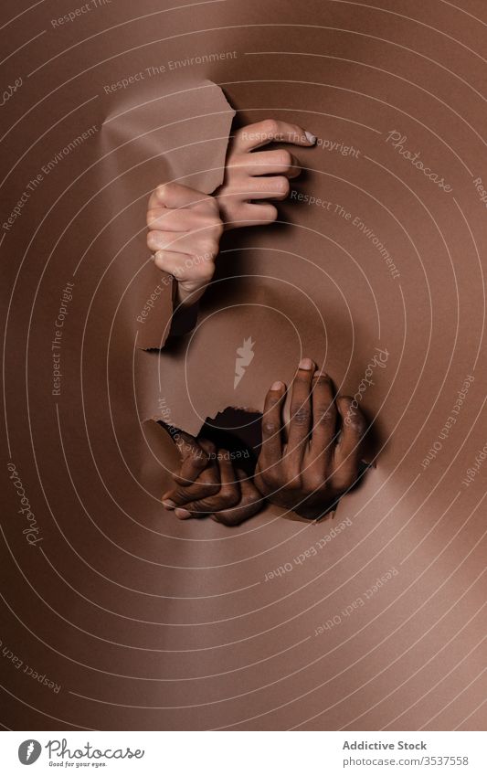 Anonymes gemischtrassiges Ehepaar durch Papiervorhang geplatzt Paar Hand Golfloch Gardine zeigen Zusammensein Finger Freude Freizeit Spaß Arme Handfläche