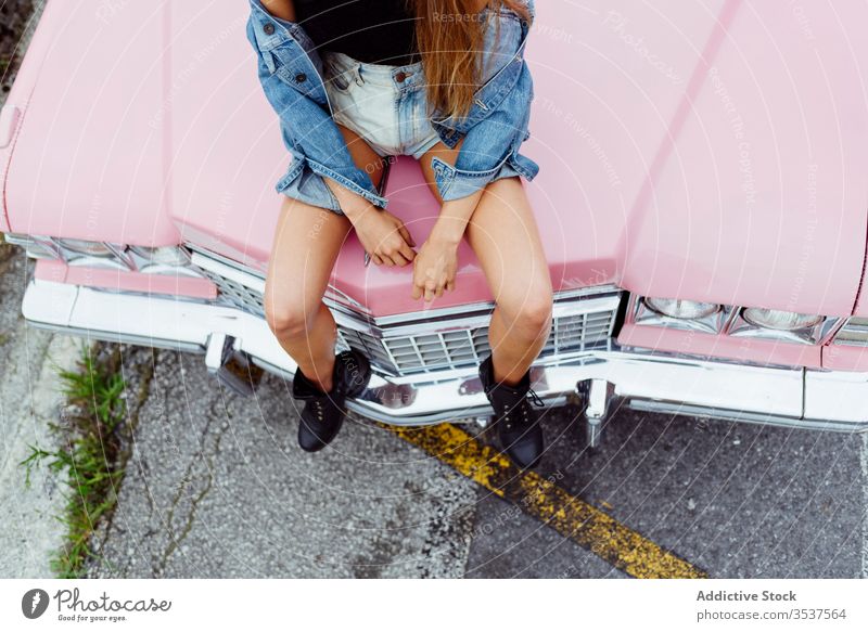 Unbekanntes blondes Mädchen auf der Motorhaube eines rosa Oldtimers auf der Straße sitzend Frau jung Zopf Sitzen Bürgersteig PKW klassisch alt Grunge Sommer