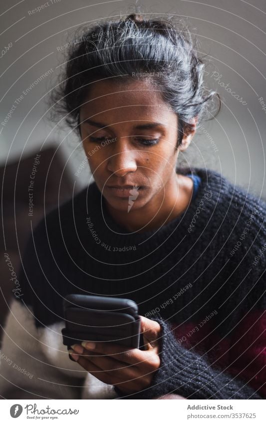 Seriöse junge ethnische Dame surft auf Smartphone Frau benutzend Komfort gemütlich Pullover Liege ruhen heimwärts Appartement Gerät Apparatur dunkles Haar