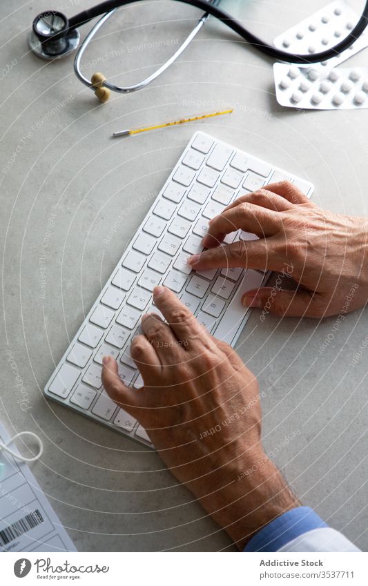 Männlicher Arzt tippt während der Fernarbeit auf der Tastatur Telemedizin Keyboard Mann Senior Verschreibung Internet online konsultieren Tippen Quarantäne