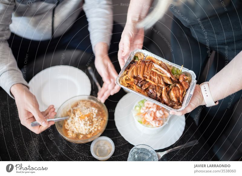 Draufsicht auf eine Frau, die einen Metallbehälter mit chinesischem Essen in der Hand hält, und ihren Partner, der zum Essen bereit steht, in unkonzentriertem Hintergrund. Gemeinsames Essen zu Hause während der Isolation durch Covid19.Familie