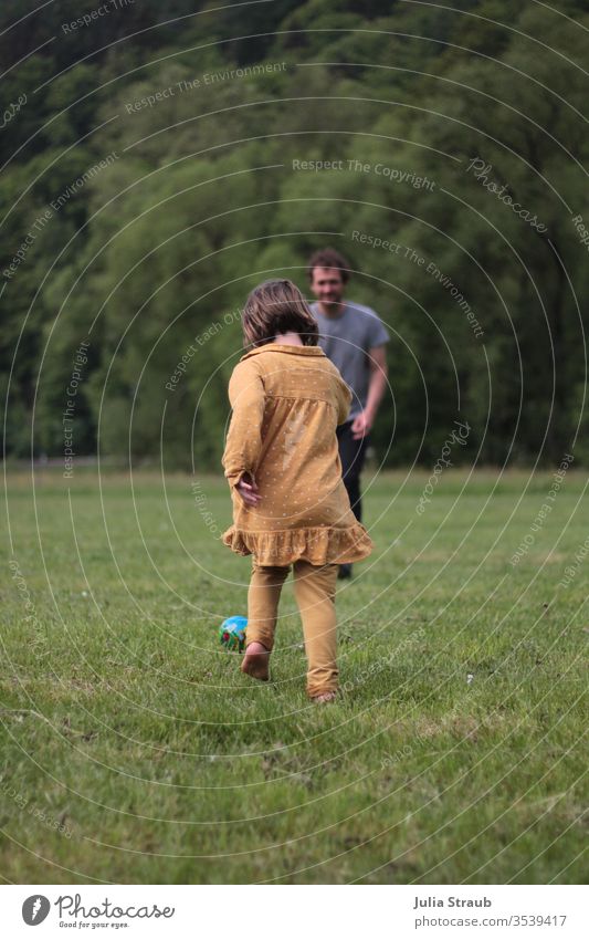 Kind spielt Fußball mit einem Mann auf einer Wiese Vater Mädchen Platz Bäume Wald Waldrand Kleid Ball senfgelb Spielen rennen bewegen Dynamisch Barfuß