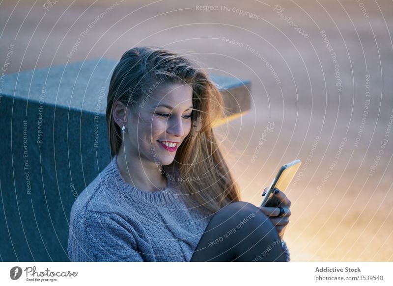 Lächelnde Frau surft auf einem Smartphone, während sie sich bei Sonnenuntergang im Park ausruht Browsen ruhen Glück heiter froh benutzend zuschauend