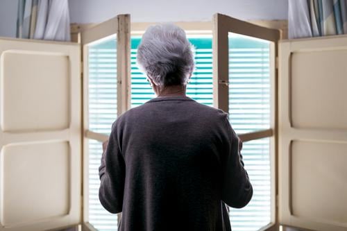 Grauhaarige Frau steht zu Hause vor dem Fenster heimwärts Senior einsam Quarantäne Coronavirus Fensterladen offen allein alt Einsamkeit Konzept gealtert