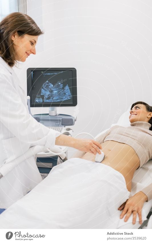 Ärztin, die eine Ultraschalluntersuchung bei einer Frau durchführt Arzt geduldig Sonogramm Klinik fruchtbar Schwangerschaft Frauen Lächeln Medizin Bauch