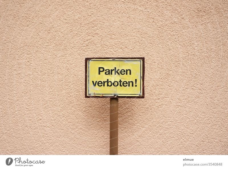 gelbes Schild mit schwarzer Schrift "Parken verboten!" vor einer altrosa Wand Parkverbot Parkschild Bußgeld Hinweisschild Verbot Putz Aufsteller Autofahren