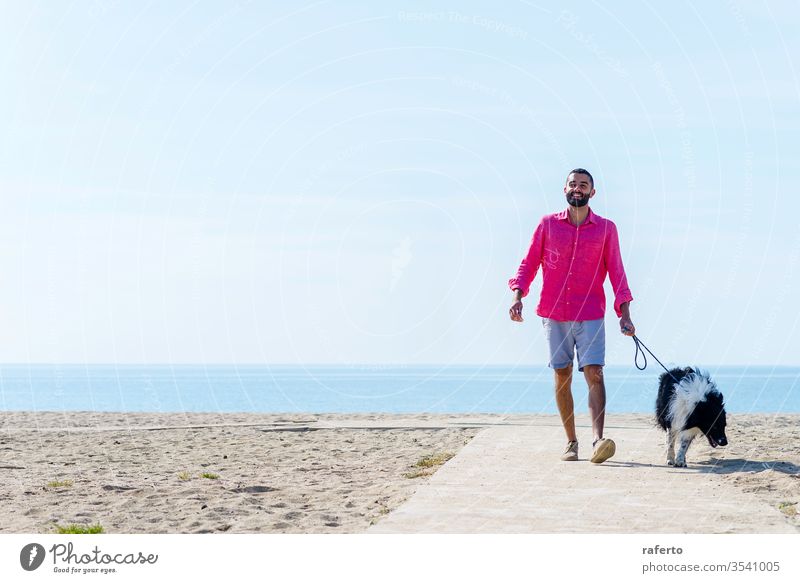 Junger bärtiger Mann geht mit angebundenem Hund am Strand spazieren Person laufen Haustier Tier im Freien Freundschaft männlich MEER Erwachsener Natur Sommer