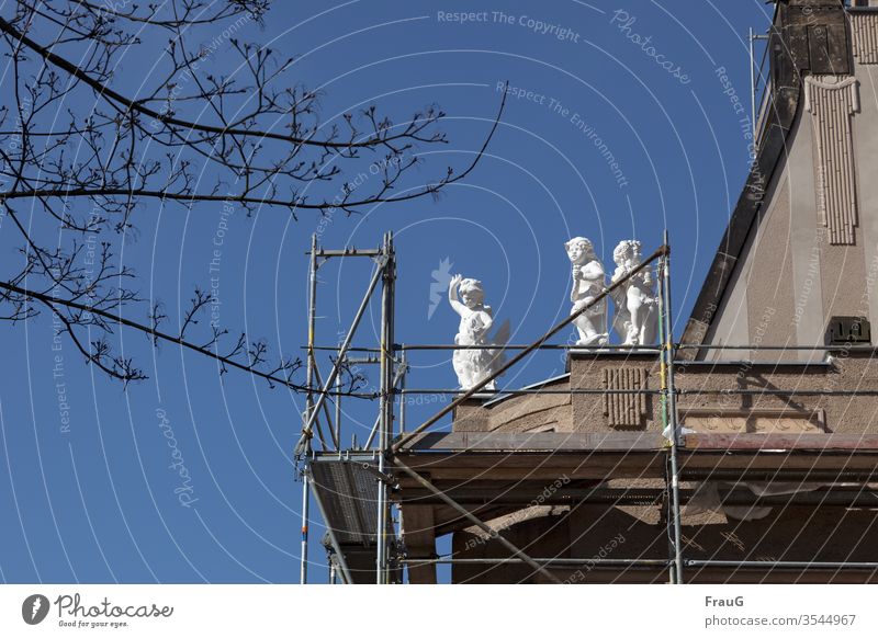 winkender Engel | Kunst am Bau Gebäude Haus Fassade Gerüst Baugerüst Sanieren Baustelle Figuren drei Flügel Teufel weiß Zweige blauer Himmel