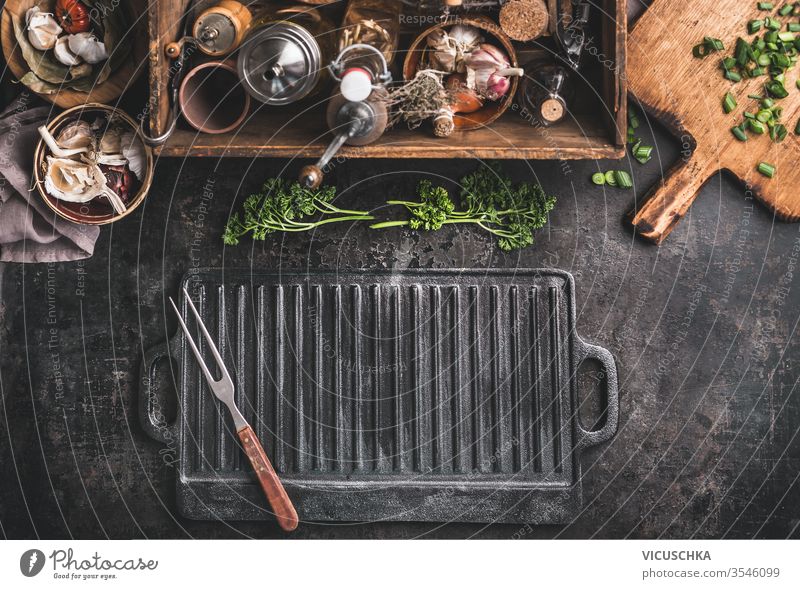 Grill- oder BBQ-Hintergrund mit leerer gusseiserner Grillgitterplatte und Fleischgabel auf rustikalem Küchentisch. Holzkiste mit Gewürzen. Küchenutensilien.Ansicht von oben. Platz für Design