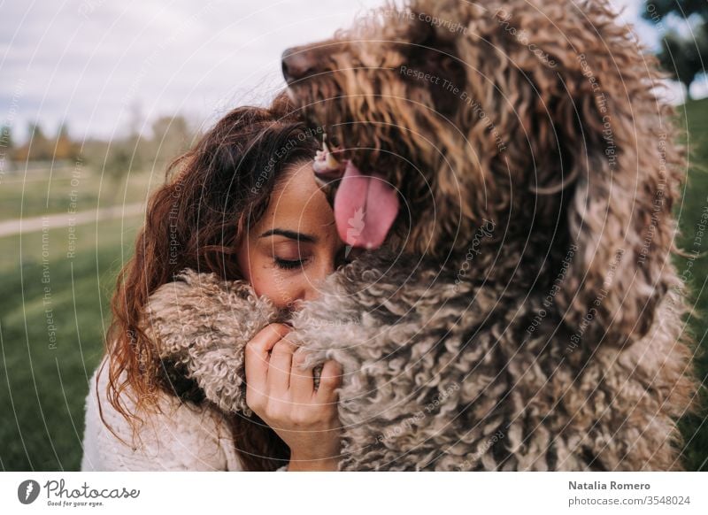Eine schöne Frau ist mit ihrem Hund auf der Wiese. Sie umarmen sich. Sie hat ihre Augen geschlossen, während das Hündchen in die Ferne schaut. Sie genießen ihre Gesellschaft. Das Haustier ist ein spanischer Wasserhund.