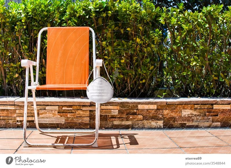 Oranger Stuhl mit schützender Gesichtsmaske und Baumlandschaft covid-19 Virus Pandemie Konzept Gesundheit Krankheit Mundschutz Schutz während anhaben Wasser