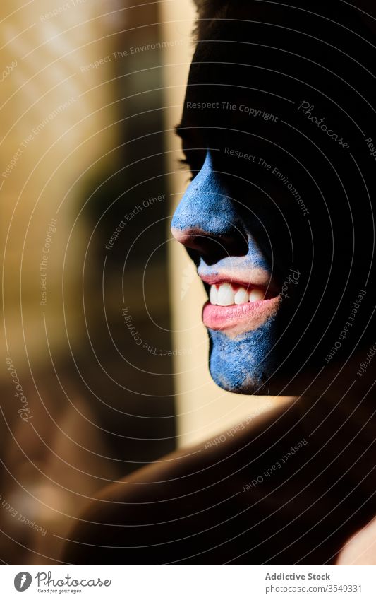 Lächelnde Frau mit blauer Tonmaske auf dem Gesicht Zahnfarbenes Lächeln Hautpflege Gesichtsbehandlung Schönheit Glück Inhalt Sonnenlicht verträumt nachdenklich