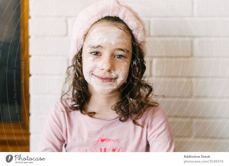 Süßes Mädchen mit weißer Gesichtsmaske Kind Pyjama Hautpflege Lächeln Pflege Stirnband Porträt froh wenig rosa natürlich heimwärts Kosmetik Gesundheit niedlich