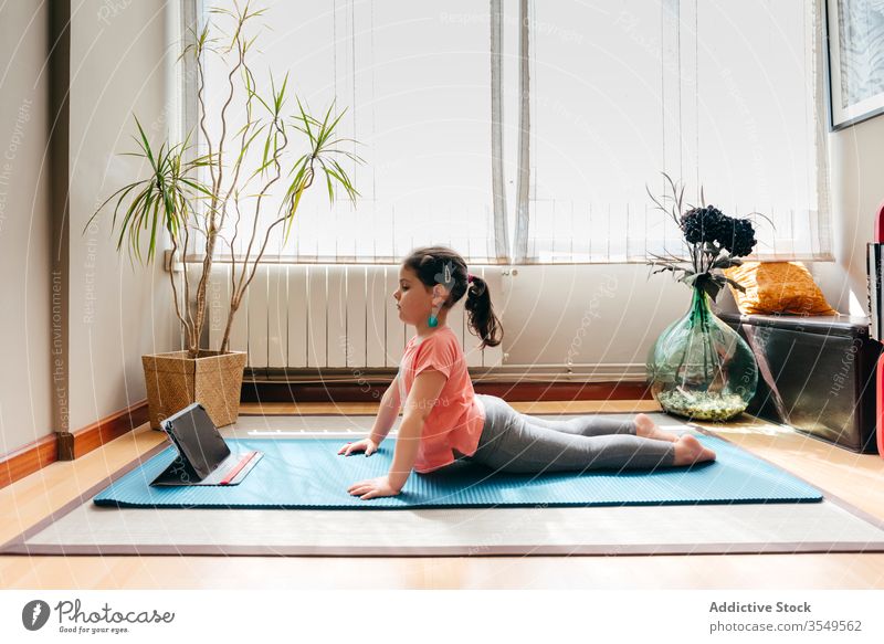 Kleines Mädchen, das Yoga in Kobra-Pose praktiziert Kind Asana üben heimwärts Tablette bhujangasana online beweglich Dehnung wenig Unterlage Gleichgewicht