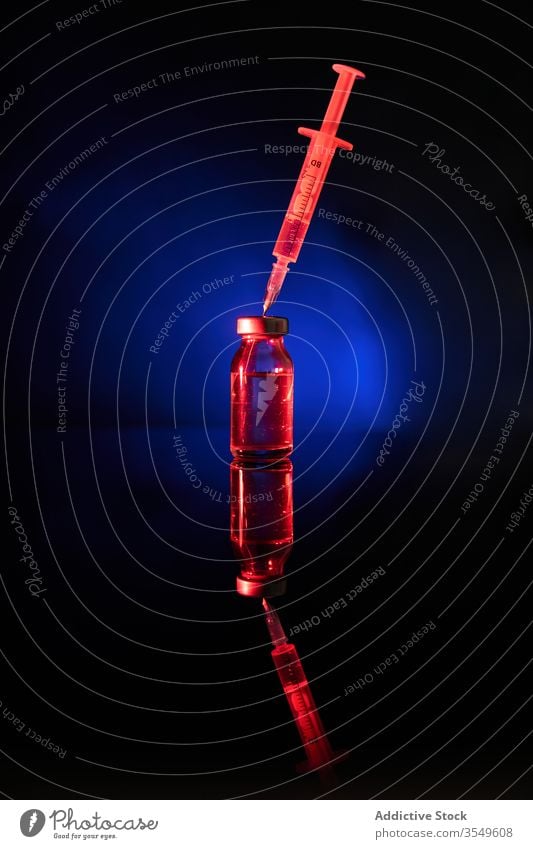 Spritze mit Nadel im dunklen Raum in der Kappe der Flasche Impfstoff Medikament Kur Bund 19 Infektion Virus Coronavirus neonfarbig leuchten durchsichtig