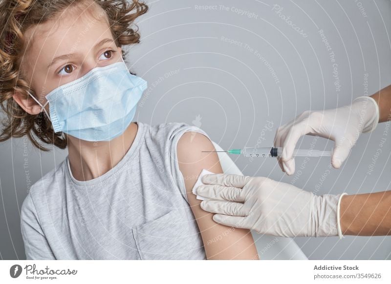 Anonymer Arzt hält Jungen während der Injektion in der Klinik an der Schulter Impfstoff Einspritzung Leckerbissen Spritze Medizin Handschuh geduldig