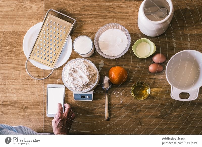 Frau benutzt Mobiltelefon während der Zubereitung von Gebäck Bestandteil backen Smartphone Skala Browsen Gewicht Teigwaren Küche vorbereiten Koch Hand Rezept