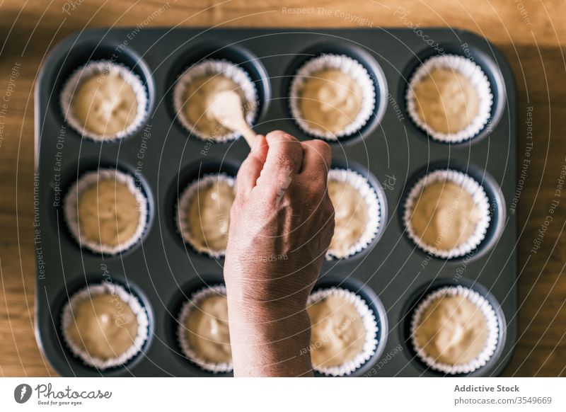 Nutzpflanzenfrau füllt Muffin-Behälter mit Teig Tablett Teigwaren besetzen Hausfrau Muffin-Gehäuse eingießen Löffel Frau Cupcake-Einlage Küche Senior heimwärts