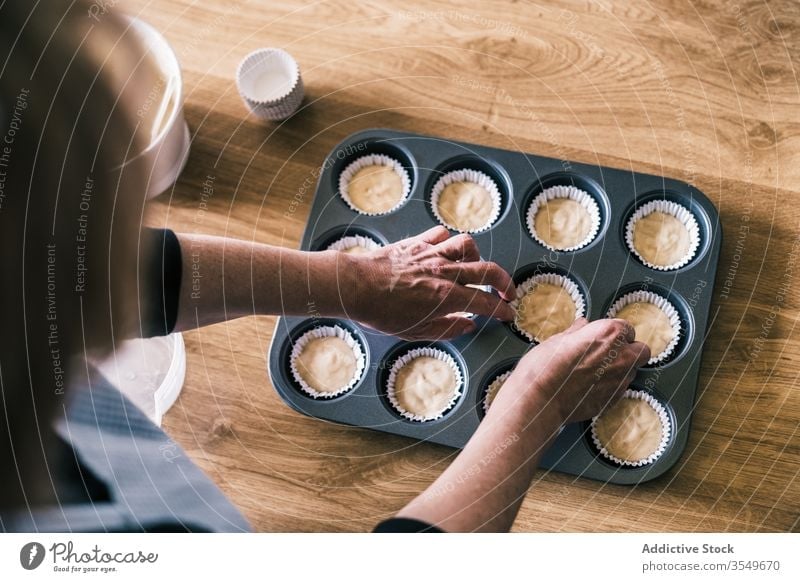 Senior-Hausfrau bereitet Teig in Muffin-Fällen zu eingießen Teigwaren Muffin-Gehäuse besetzen Tablett Küche Frau heimwärts Konditor Koch vorbereiten Papier