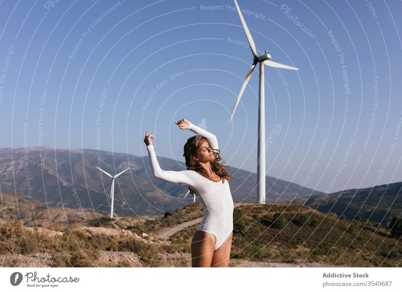 Zarte Frau tanzt allein in der Nähe des Windparks auf sonnigem Feld Tanzen Landschaft sinnlich Natur Ökologie schlank Stil hochreichen alternativ Windmühle