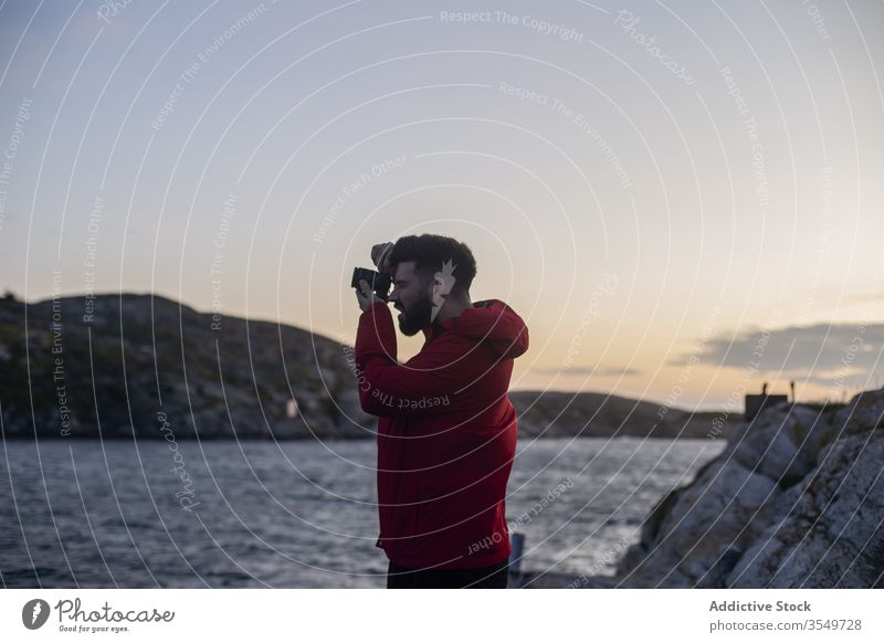 Mann fotografiert mit einer Fotokamera an der Meeresküste fotografieren felsig Fotograf Küste Klippe Sonnenuntergang Abend MEER Natur Fotoapparat Ausflug reisen