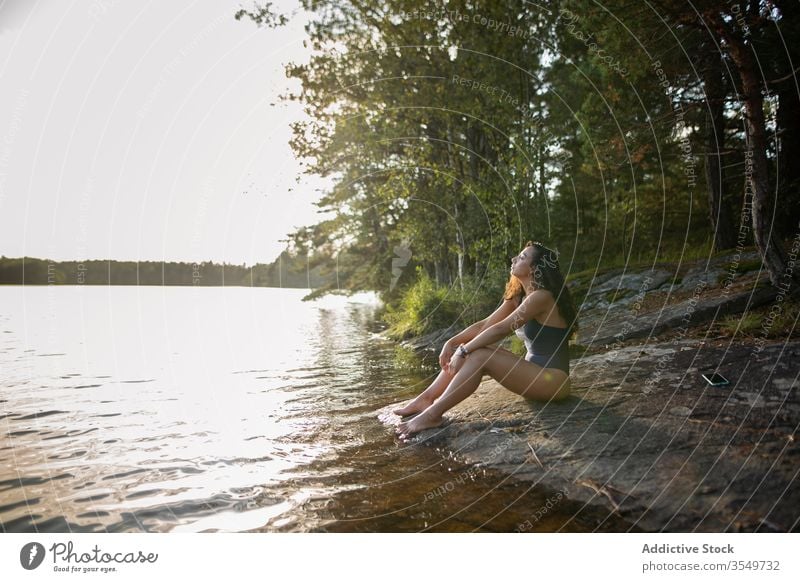 Frau im Badeanzug sitzt im Sommer am Seeufer Ufer genießen Landschaft felsig Küste Wald majestätisch sitzen ruhig Windstille Gelassenheit Harmonie friedlich
