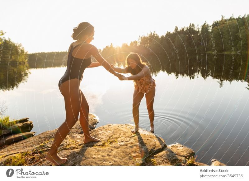 Freundinnen in Badeanzügen am Seeufer bei Sonnenuntergang Händchenhalten Ufer Badeanzug Sommer Urlaub Zusammensein Frauen jung sich[Akk] entspannen Windstille