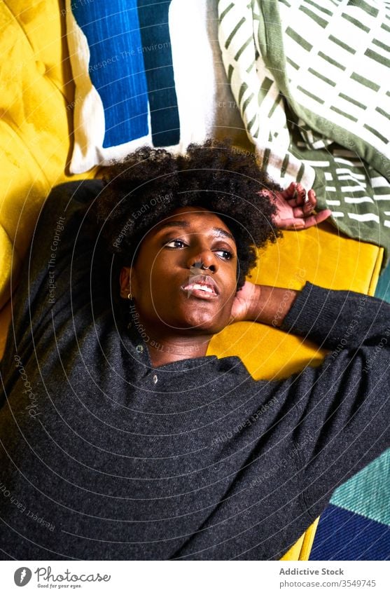 Junge schwarze Frau ruht auf farbenfrohem Sofa heimwärts Lügen gelangweilt besinnlich Design nachdenklich träumen jung Afroamerikaner lässig Liege ethnisch