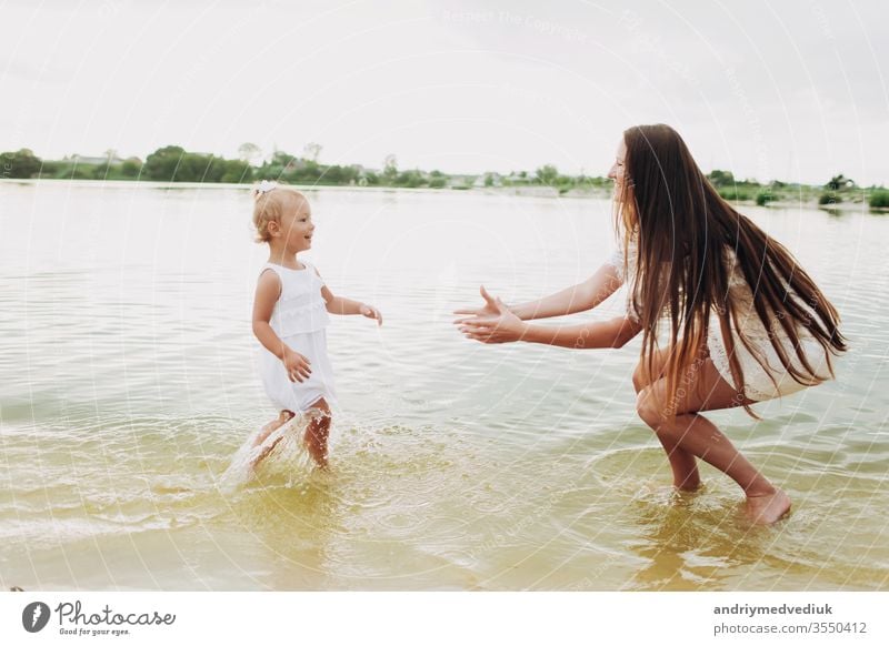 schöne Mutter mit kleiner Tochter haben Spaß und spielen in der Nähe des Sees. Das Konzept der Sommerferien. Tag der Mutter, Tag des Babys. Zeit miteinander verbringen. Der Blick der Familie. Sonnenlicht. selektiver Fokus