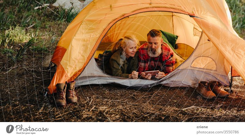 Kaukasisches älteres Paar surft auf dem Telefon, während es im Schlafsack im Zelt liegt Smartphone Technik & Technologie Lächeln verbunden Wald Internet Browsen