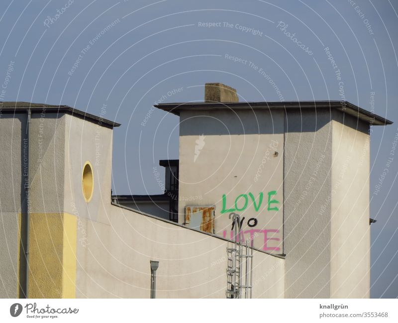 Gebäude mit zwei Türmen, auf einem ein Graffiti LOVE NO HATE Liebe Wand Mauer Feuerleiter hoch Flachdach Blauer Himmel Außenaufnahme Farbfoto Menschenleer