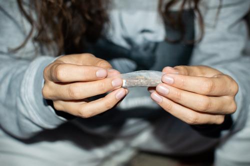 Junge Frau im Trainingsanzug, die nachts einen Marihuana-Joint auf der Straße rollt. Einzelheiten über Hände, die eine Cannabis-Zigarette drehen. Gelenk rollen