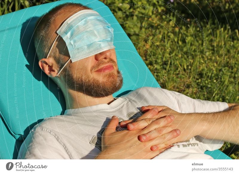 junger Mann liegt auf Sonnenliege und hat eine Atemschutzmaske vor den Augen Schutzmaske Augenschutz Hygiene Sonnenschutz Vorsichtsmaßnahme Gefahr erholen