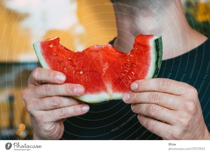 Ein Mann hält ein angebissenes Stück Wassermelone in der Hand essen beißen lecker Sommer rot frisch reif fruchtig Ernährung saftig Essen