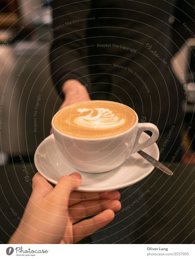 Ein Café Latte mit Schwan-Latte-Kunst wird vom Barista an den Kunden übergeben Kaffee Kaffeetasse Latte Art Kaffeekultur Kaffeehaus flach weiß Koffein