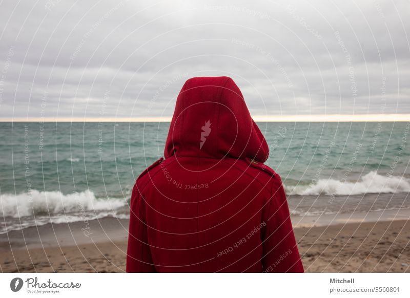 Eine Person in leuchtend roter Jacke schaut auf das Meer Ansicht Mantel Blick Sehnsucht Fernweh reisen Tourismus Urlaub Flucht Wellen Wasser MEER See pulsierend