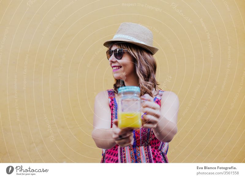 Porträt einer jungen kaukasischen Frau im Freien über gelbem Hintergrund, die eine Tasse gesunden Orangensaft genießt. sommerzeit Großstadt Sommer Gesundheit