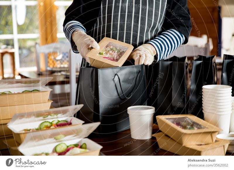 Restaurantmitarbeiter mit Schutzmaske und Handschuhen, die in Lebensmittelkartons verpacktes Essen zum Mitnehmen verpacken. Lebensmittellieferdienste und kontaktloser Online-Einkauf von Lebensmitteln.