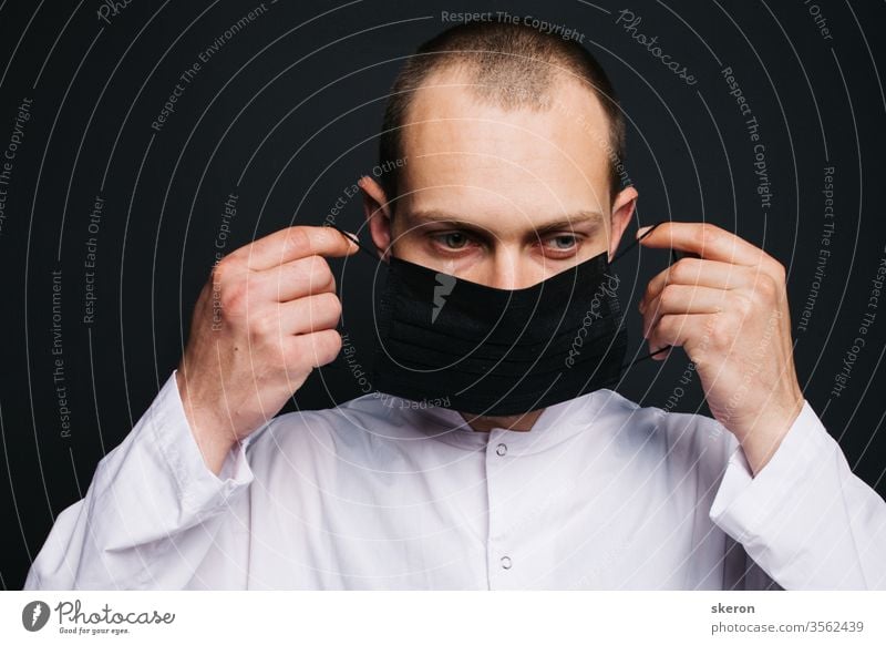junger Arzt mit kurzen Haaren im Ärztekittel trägt eine schwarze Schutzmaske. männlicher Laborant im Schutzanzug bei der Arbeit mit Patienten mit Coronavirusinfektion während der Pandemie.