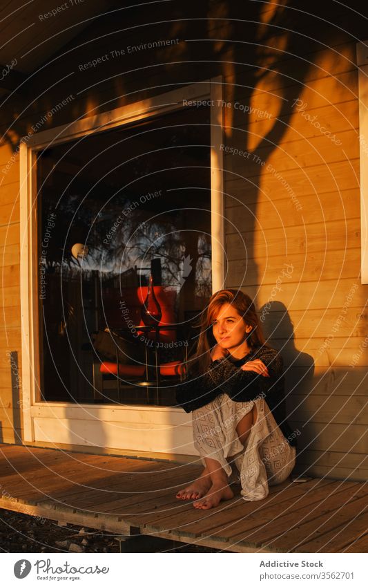 Entzückte Frau bewundert Sonnenuntergang auf der Terrasse einer Holzhütte bewundern sich[Akk] entspannen Veranda Haus Freude Barfuß Kabine Gelassenheit Kälte