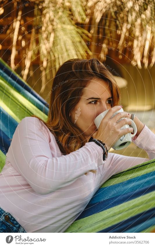 Entspannte Frau mit Tasse Kaffee in Hängematte sich[Akk] entspannen Heißgetränk Windstille trinken Barfuß Hof genießen Sommer Feiertag Urlaub Wochenende Becher