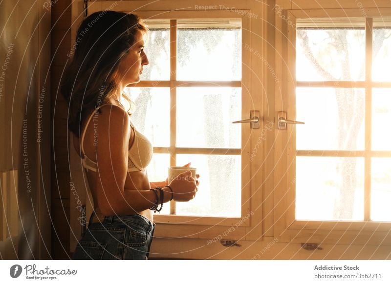 Entspannte Frau am Morgen mit Kaffee am Fenster sich[Akk] entspannen genießen Wochenende Kabine Gelassenheit Getränk Jeanshose BH Tasse heiß trinken Heißgetränk