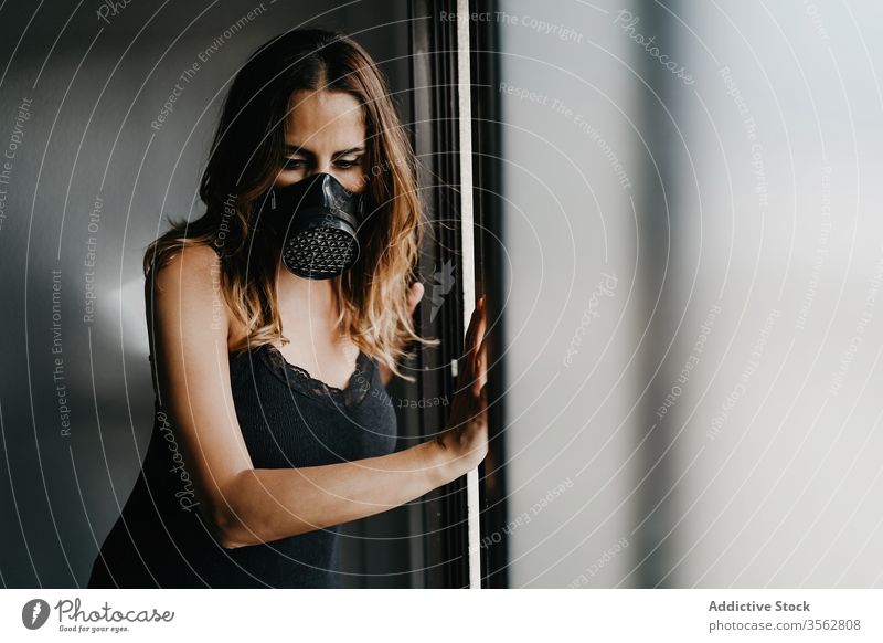 Junge Frau mit Atemschutzmaske steht an Glaswand Mundschutz Isolation COVID Coronavirus Konzept verhindern Schloss Selektiver Fokus behüten einlochen traurig