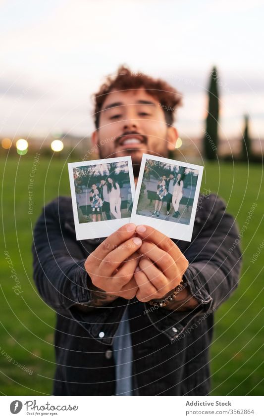 Glücklicher Mann zeigt Fotos von Familie zeigen Bild Liebe Park Gedächtnis heiter lässig Partnerschaft Lächeln manifestieren männlich Fotografie Gras positiv