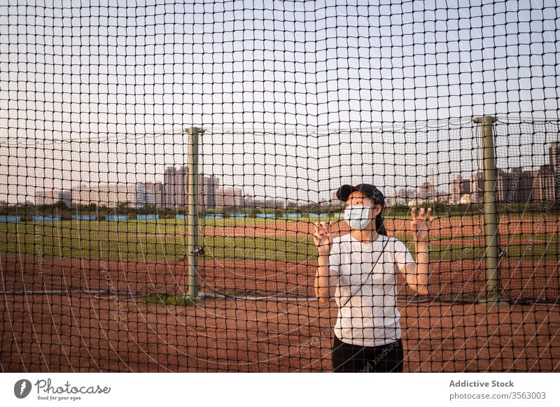 Junge Frau mit Schutzmaske steht hinter Netzzaun auf Sportplatz Mundschutz Coronavirus Sportpark Zaun Einschränkung verhindern behüten COVID jung sportlich
