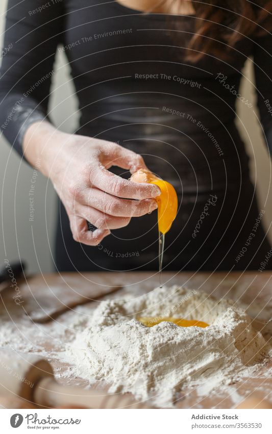 Ernte-Hausfrau, die bei der Teigherstellung dem Mehl Eier hinzufügt hinzufügen roh Pause Frau Küche Koch Teigwaren Gebäck vorbereiten Nudelholz Bestandteil